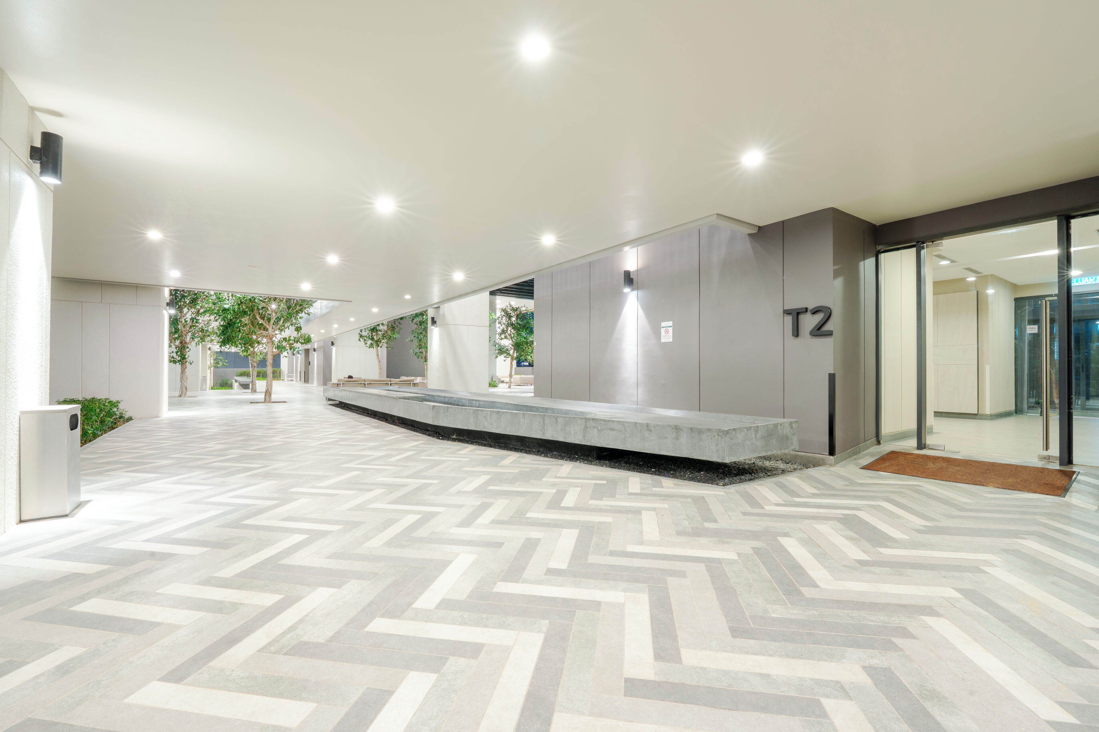 Een moderne lobby met een visgraat vloerpatroon, een receptiebalie en een glazen deur met de tekst 