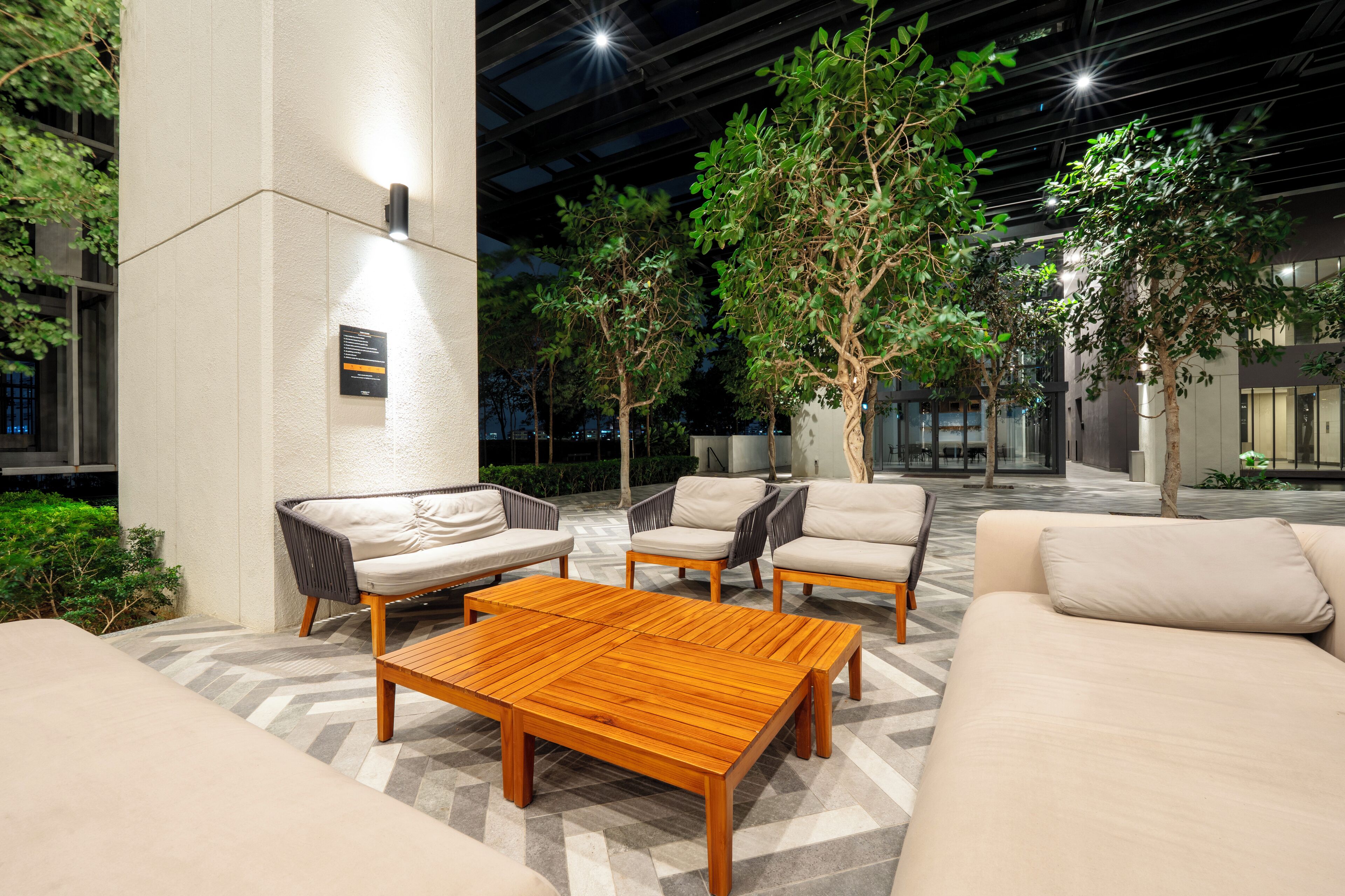 Een moderne, overdekte lounge met zitplaatsen en een houten bijzettafeltje.