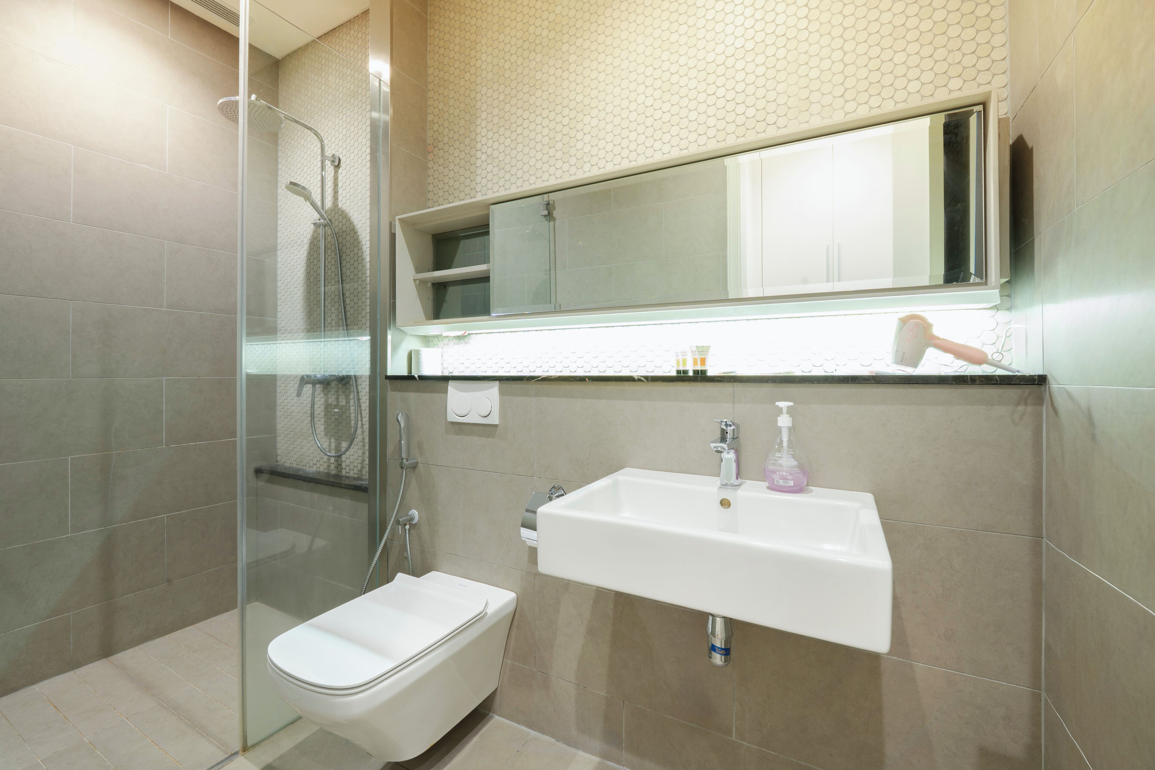 Un baño moderno con ducha de vidrio, lavabo blanco y espejo sobre él.