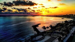 A coastal sunset view with a marina and buildings in the background. - Luxury Apartment 3BR & Full Sea View (Marsa Matrouh)