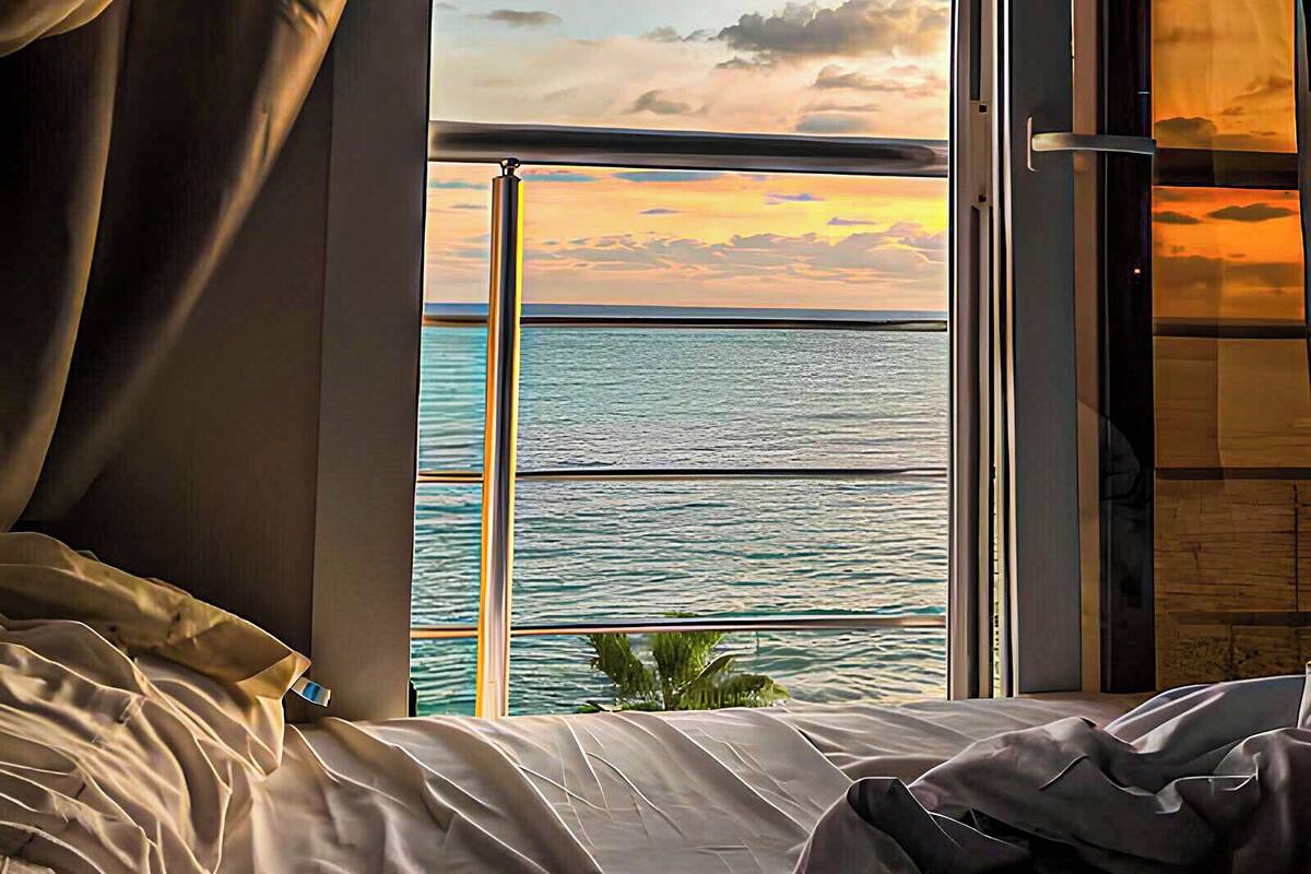 Una habitación con cama, ventana con cortinas y vista al mar y al cielo.
