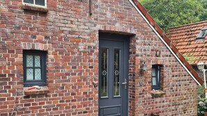 A brick building with a dark door, two windows, and a small porch area. - The Kirsche - Rustic sleeping barrel in East Frisia (Holtgast)