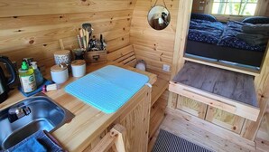 A compact wooden cabin with a kitchenette, a small sink, and a window overlooking a snowy landscape. - The Kirsche - Rustic sleeping barrel in East Frisia (Holtgast)