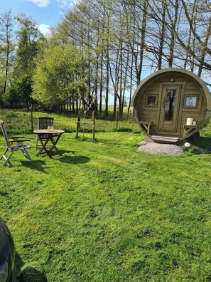 A spherical wooden cabin with a door and windows, surrounded by a grassy area with a table and chairs. - The Kirsche - Rustic sleeping barrel in East Frisia (Holtgast)