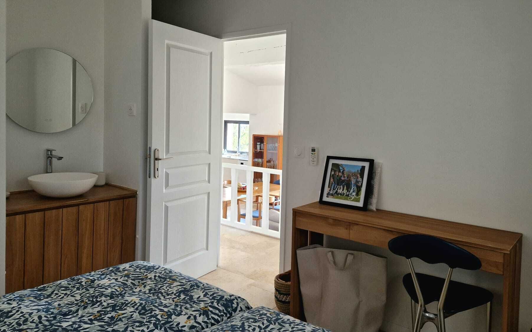 A bedroom with a bed, a bedside table, a mirror, and a door leading to a dining area.