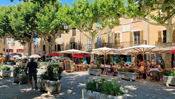 An outdoor café area with tables and chairs under umbrellas, surrounded by trees and buildings. - Charming family villa in Tourtour. 40 minutes from the Côte d'Azur. (Tourtour)