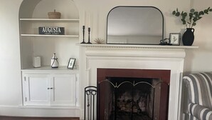 A living room with a white fireplace, a mantel with decorative items, a white arched shelving unit with a sign reading "AUGUSTA EST. 1736", and a striped armchair. - Welcome to Augusta. This beautiful and home has lots of Southern Charm. (Augusta)