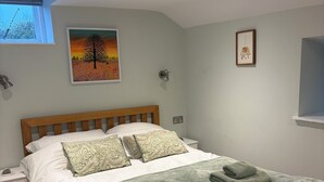Un dormitorio con una cama de madera, ropa de cama blanca, una manta verde y un cuadro de un árbol en la pared.