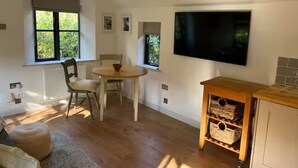 Una habitación con una mesa de comedor, sillas, un televisor montado en la pared y un armario de madera con cestas.