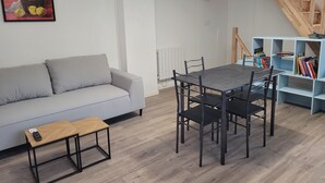 A modern living room with a grey sofa, a wooden coffee table, a dining table with chairs, a bookshelf, and a staircase. - Charming triplex near Disney  (Quincy-Voisins)