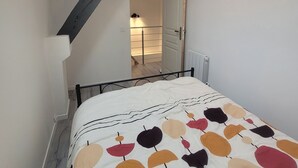 A bedroom with a sloped ceiling, a bed with a leaf-patterned duvet, a skylight, and a view of a hallway with a radiator. - Charming triplex near Disney  (Quincy-Voisins)