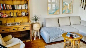 Un salon chaleureux avec une bibliothèque en bois, un canapé gris, une petite table ronde en bois et une plante en pot.