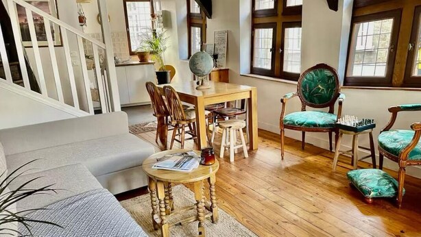 Un salon chaleureux avec un plancher en bois, un canapé, une table à manger avec des chaises et un jeu d’échecs.