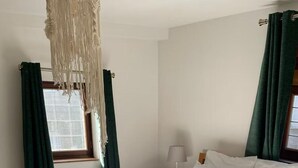 Un lit bien fait, avec du linge de lit blanc, un plaid à motifs verts et un banc en bois.