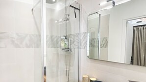 Een moderne badkamer met een glazen douchecabine, een houten wastafelmeubel met een zwarte wastafel en een grote spiegel.
