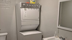 A compact laundry room with a stacked washer and dryer, a toilet, and a sink with cabinets.