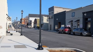 A street with buildings, a sidewalk, and a yellow tactile paving strip.