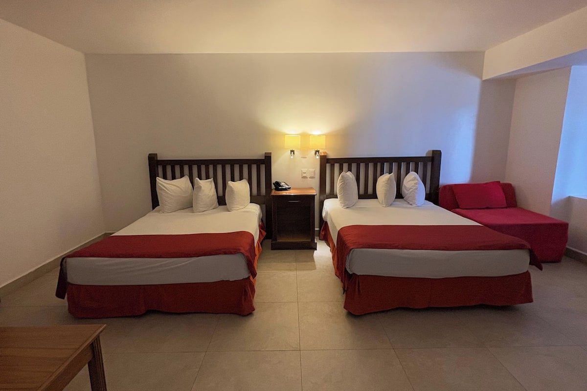 A hotel room with two beds, a nightstand with a phone, and a red chair.