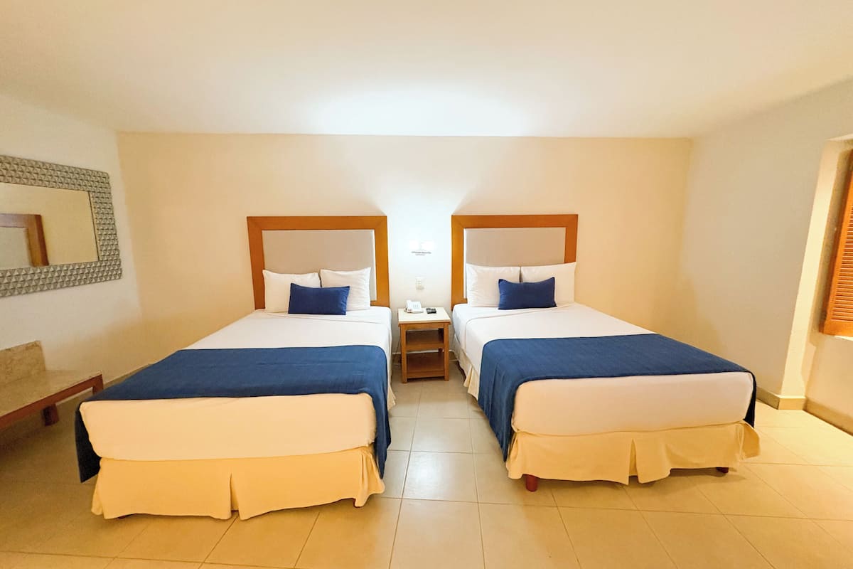 A hotel room with two beds, each with a headboard, a nightstand, and a mirror on the wall.
