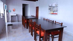 A dining area with a long wooden table and chairs, a water dispenser, and a dish rack on the wall.