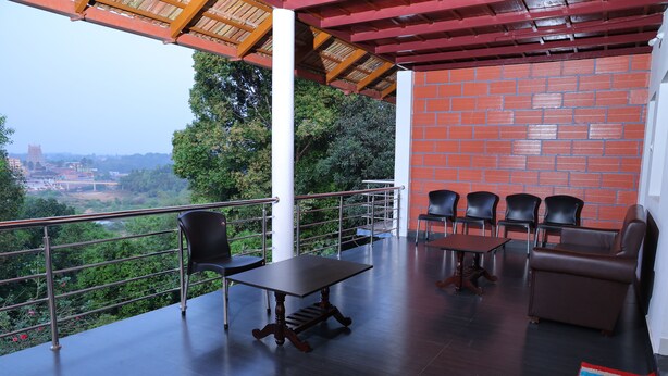 A covered outdoor seating area with a table and chairs, a sofa, and a view of greenery and buildings in the distance.