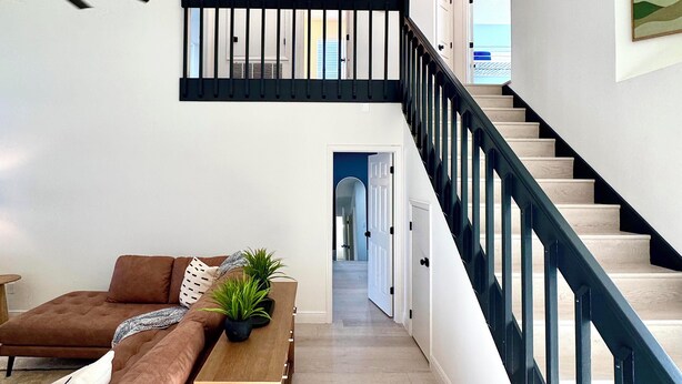 Un intérieur moderne avec un escalier, un canapé marron, une table basse en bois et une plante en pot.