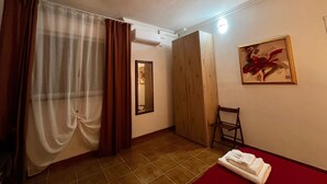 Quarto de hotel com cama, poltrona, espelho, quadro e janela com cortinas.
