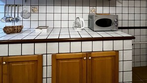 Cozinha com armários de madeira, painel de azulejos brancos e micro-ondas sobre a bancada.