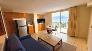 Ett modernt hotellrum med en soffa, ett matbord med stolar, ett köksutrymme och en balkong med utsikt.