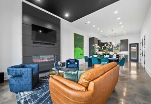A modern living room with a fireplace, blue chairs, a leather sofa, and a dining area with teal chairs.