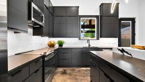 A modern kitchen with dark cabinetry, a central island, and a window with a view. - Modern Retreat with Rooftop and Lake Access (Hot Springs)