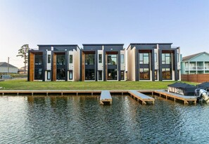 A modern building with a flat roof, large windows, and a dock extending into a body of water. - Modern Retreat with Rooftop and Lake Access (Hot Springs)