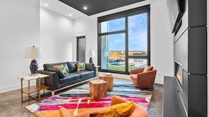 Een moderne woonkamer met een bank, fauteuils, een open haard en een groot raam met uitzicht.