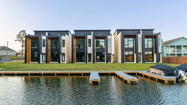 Een modern gebouw met een plat dak, grote ramen en een steiger die in het water uitkomt.