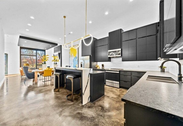 Une cuisine moderne dotée d’un îlot central, de meubles de rangement aux couleurs sombres et d’une grande fenêtre.