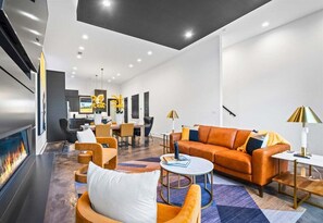 A modern living room with a fireplace, orange sofa, and a dining area in the background. - Modern Retreat with Rooftop and Lake Access (Hot Springs)