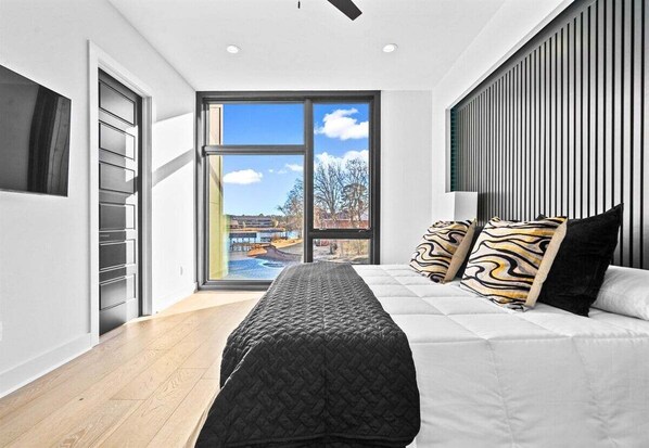 Une chambre moderne avec une grande fenêtre, un lit agrémenté d’oreillers à motifs et un banc.