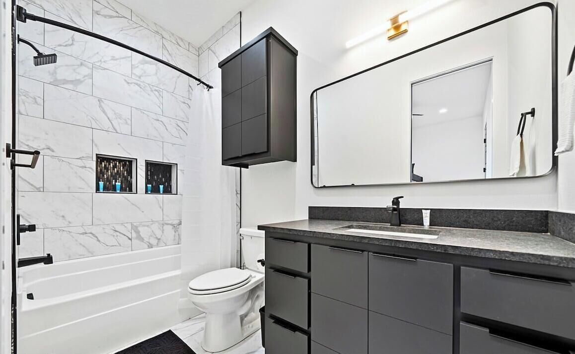 Un baño moderno con ducha, inodoro y tocador con un espejo grande.