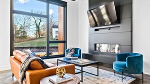 A modern living room with a large window, a fireplace, and a flat-screen TV mounted on the wall. - Modern Retreat with Rooftop and Lake Access (Hot Springs)