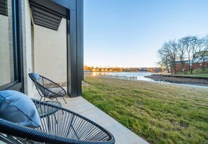 A patio with two black wire chairs and a view of a body of water and buildings in the distance.