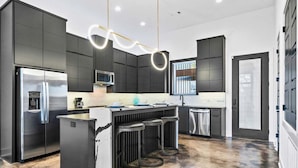 A modern kitchen with dark cabinetry, stainless steel appliances, and a central island with bar stools. - Modern Retreat with Rooftop and Lake Access (Hot Springs)