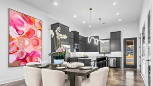 A modern kitchen with dark cabinetry, a dining area with a large abstract painting, and a view of the outdoors.
