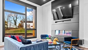 A modern living room with a large window, a fireplace, a flat-screen TV, and a sofa.