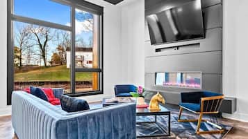 A modern living room with a large window, a fireplace, a flat-screen TV, and a sofa.