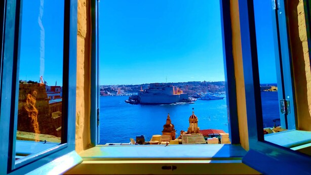 Vista a través de una ventana que muestra un cielo azul despejado, una masa de agua y edificios a lo lejos.