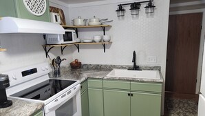 A compact kitchen with a microwave, stove, and sink. There are green cabinets and a wooden countertop.
