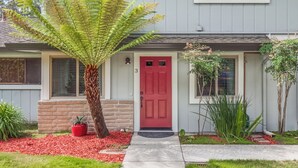 Una casa con puerta roja, un porche de ladrillo y una planta de helecho grande en el jardín delantero.
