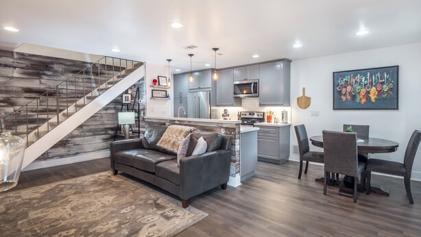 Una sala de estar moderna con un sofá gris, una escalera de madera y una cocina con armarios grises y un microondas.