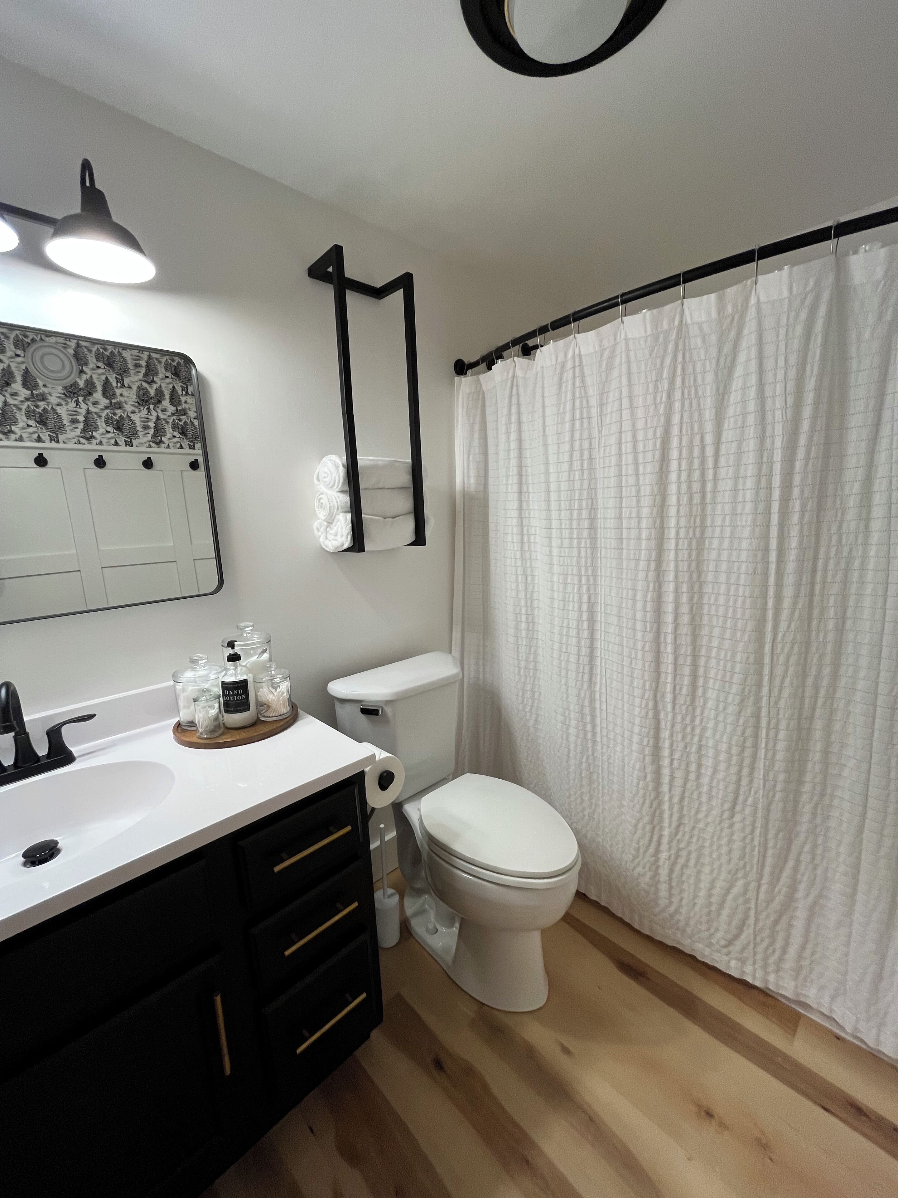 Un bagno moderno con lavandino bianco, mobili neri, un water e una tenda per la doccia.