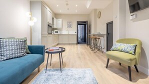 Una sala de estar moderna con un sofá, un sillón y una mesa de centro, que da a una zona de cocina con armarios y un microondas.